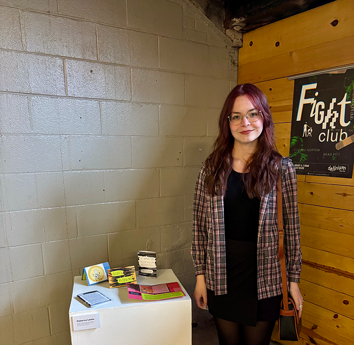 Becca Lewis standing beside her work at a exhibition